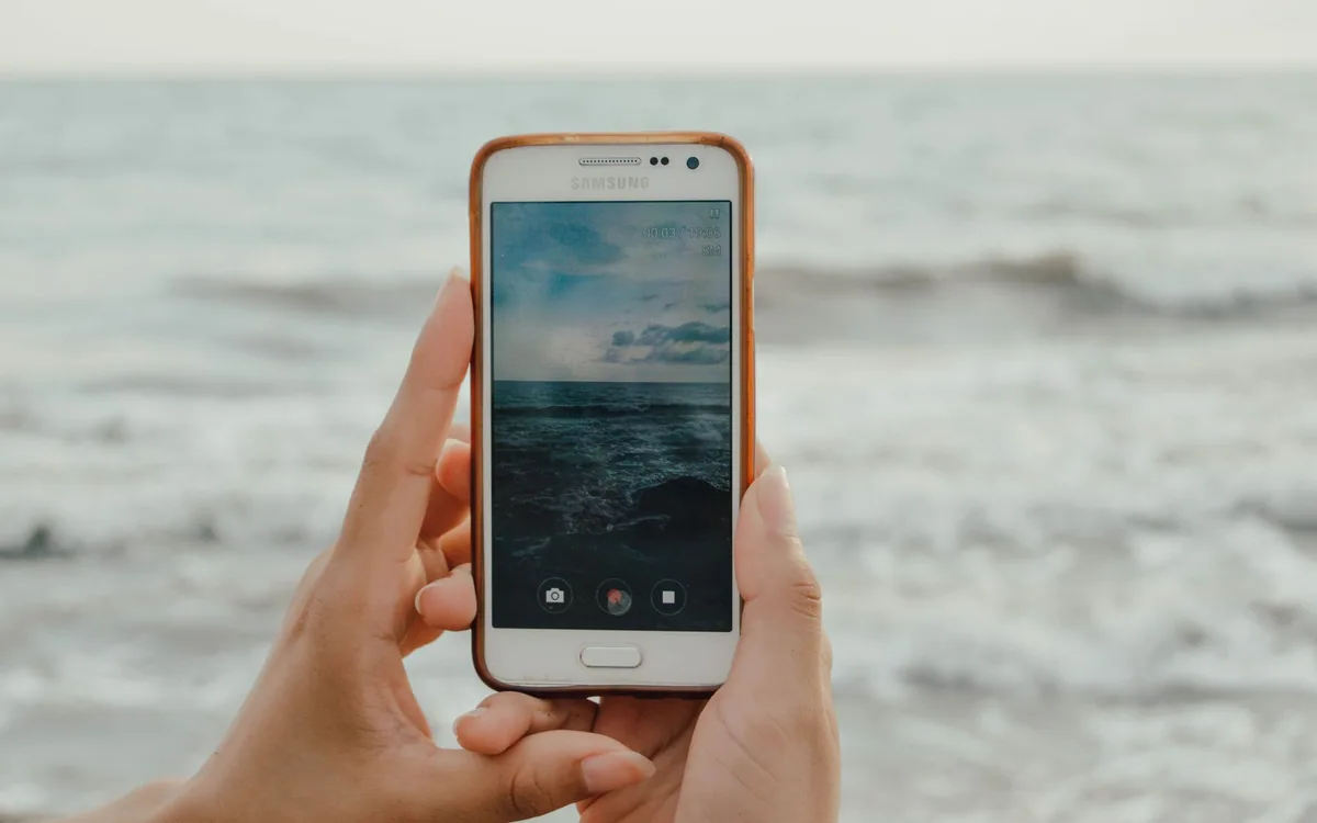 Hands use a smartphone to photograph ocean waves.