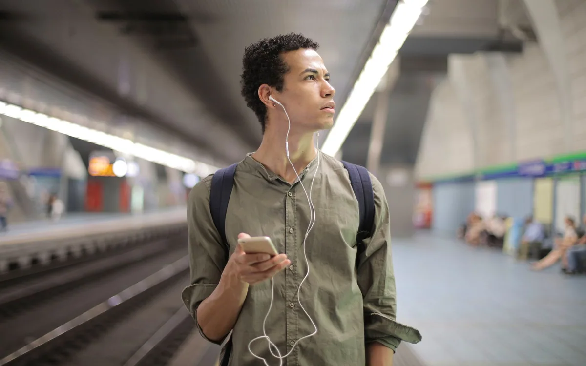 A commuter wears earphones and holds a smartphone while waiting at a subway station.