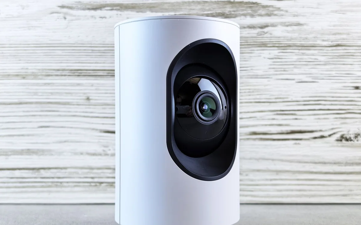 A white indoor security camera against a wooden backdrop.