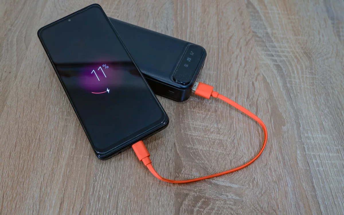 A smartphone connected to a portable power bank by an orange cable on a wooden table.