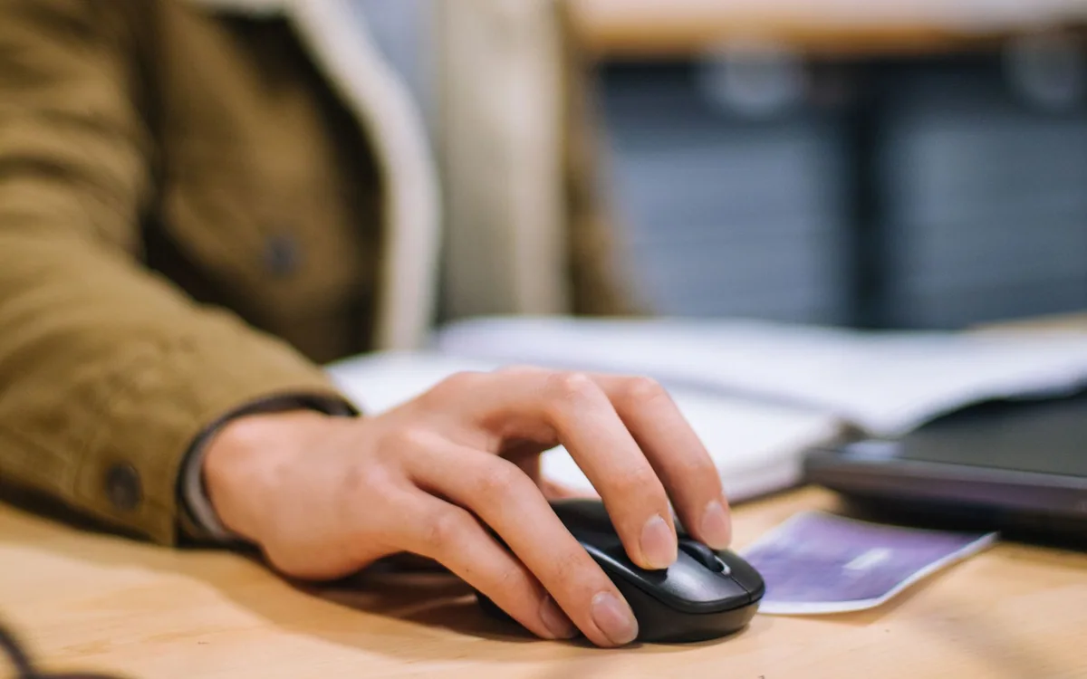 A hand operates a black wireless computer mouse at a desk.