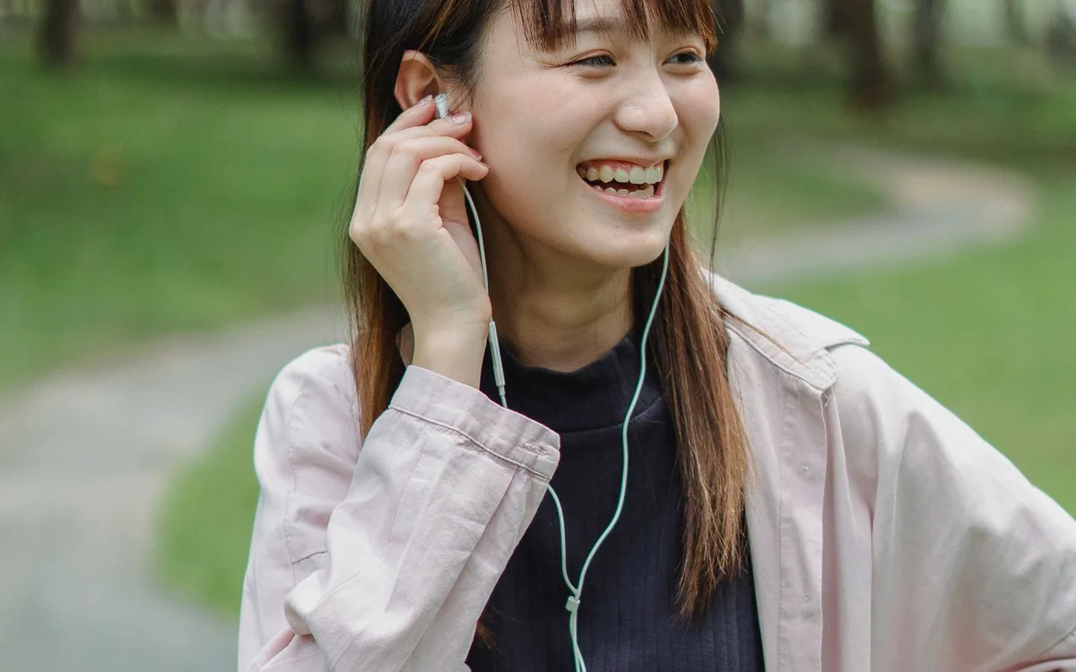 A woman wearing earphones holds a smartphone during a walk in a green park.