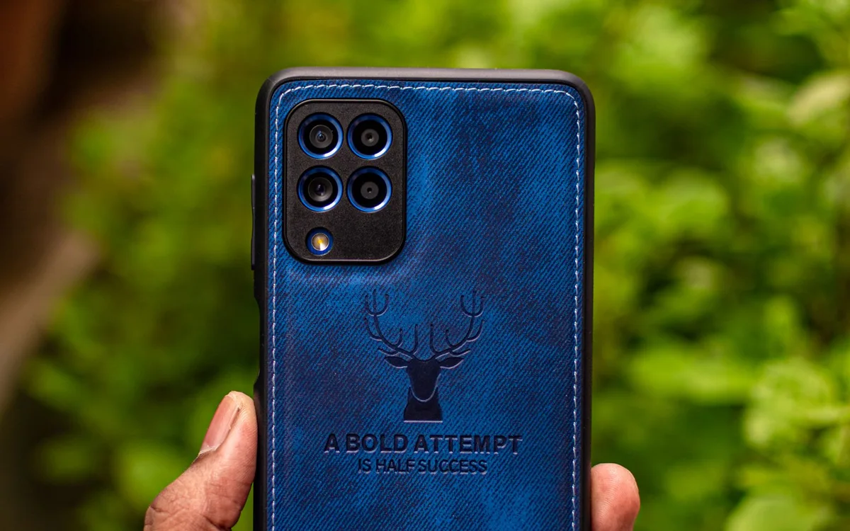 A hand holds a phone in a blue patterned case against a green outdoor background.