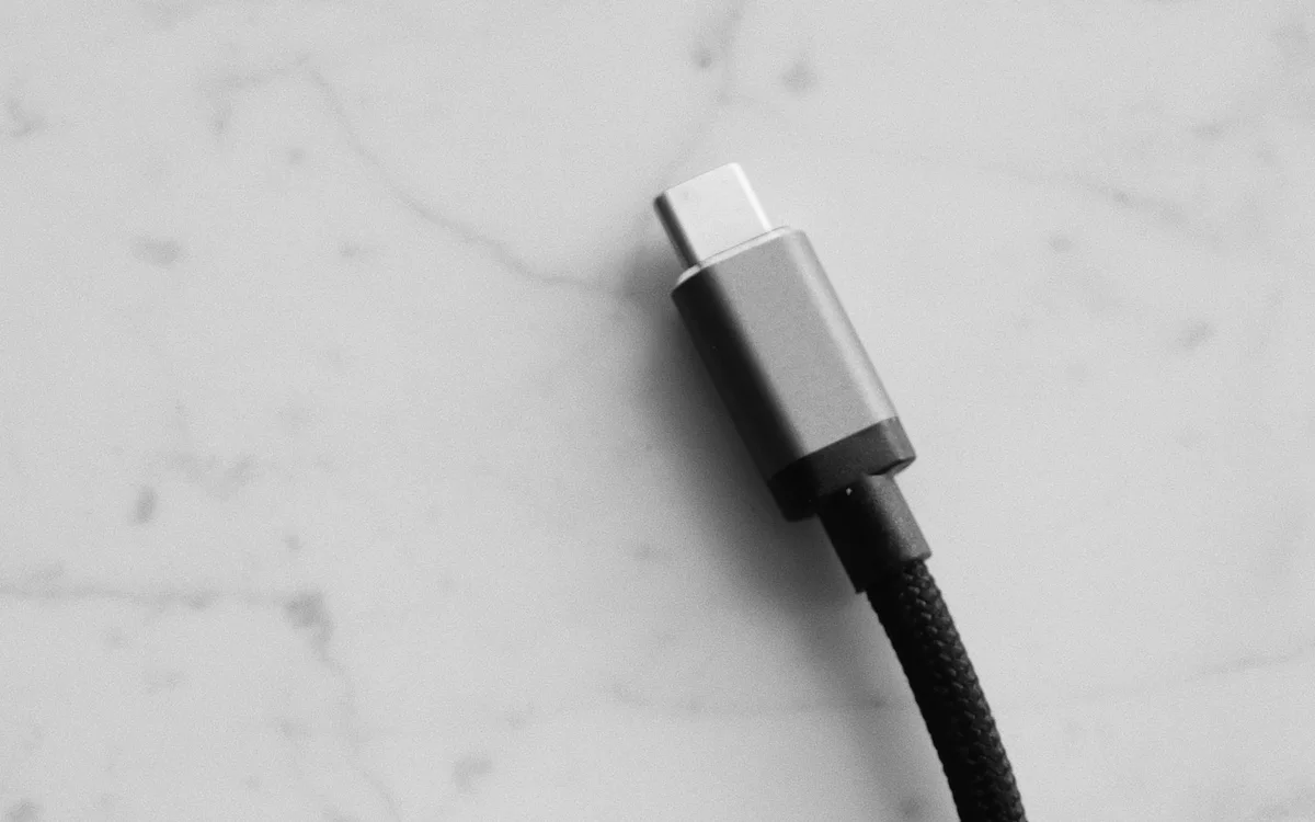 A black braided USB-C cable rests on a pale marble surface.